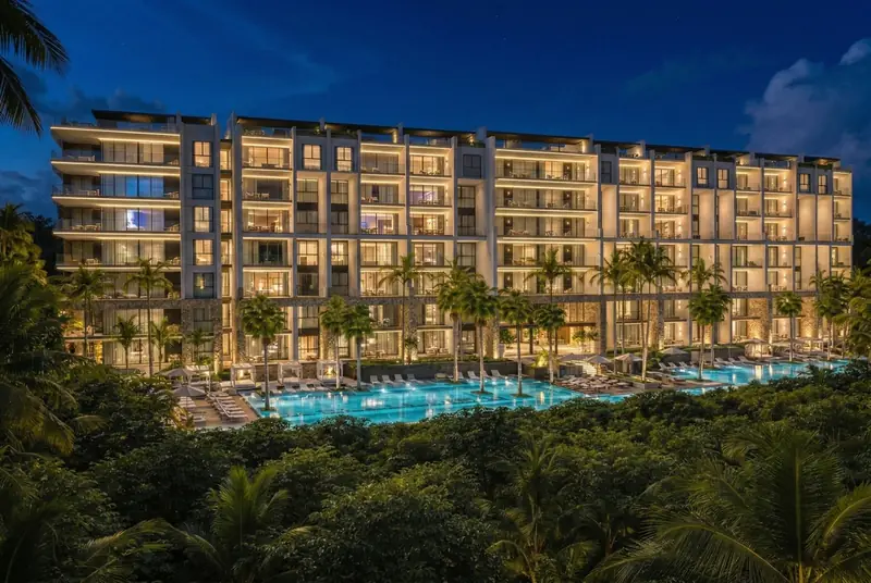 Desarrollo en preventa en Playa del Carmen de noche, con alberca iluminada entre palmeras